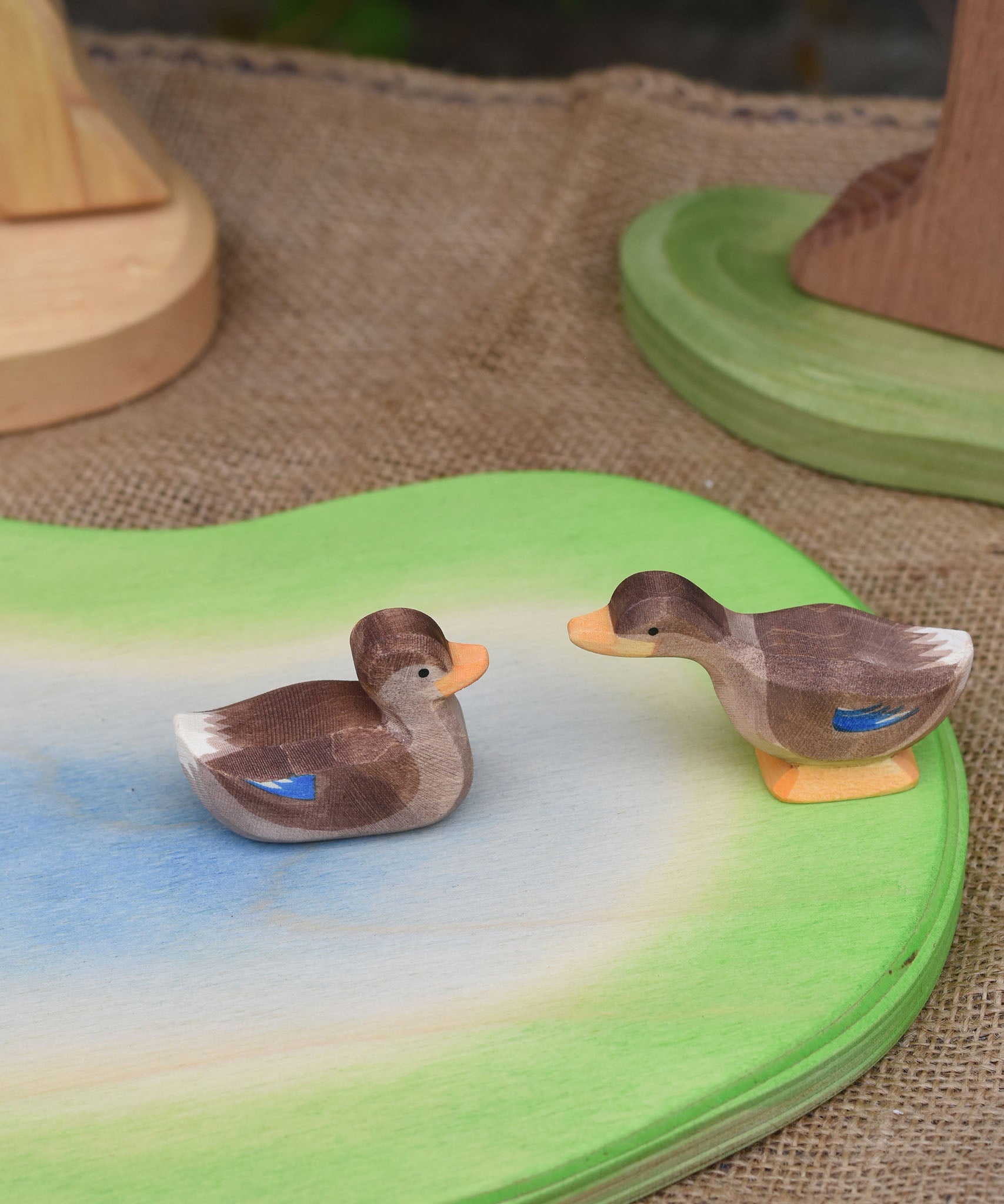 Two Ostheimer wooden ducks placed on a wooden pond scene piece. One duck is in a swimming position one is standing and has a long neck position.
