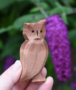 An Ostheimer brown coloured eagle owl shown in an adult's hand for scale. The owl figure is part of a large collection of expertly hand crafted wooden toys and figures here at Babipur. 