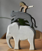 Stack of elephant, panther and baboon wooden toy figures on a wooden surface.  