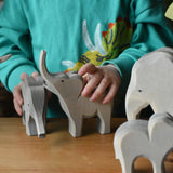 Ostheimer elephant wooden toy figures with a small trumpeting elephant figure in a child's hand in a small world play scene. 