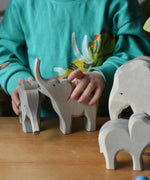 Ostheimer elephant wooden toy figures with a small trumpeting elephant figure in a child's hand in a small world play scene. 