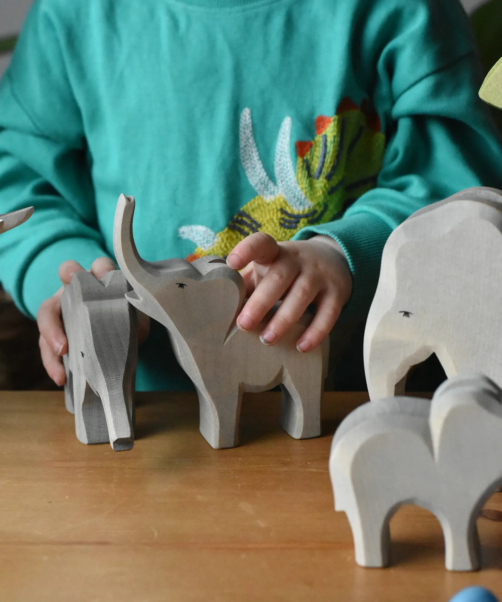 Ostheimer elephant wooden toy figures with a small trumpeting elephant figure in a child's hand in a small world play scene. 
