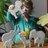 Collection of Ostheimer elephants wooden toy figures in a small world play scene with a child holding the trumpeting bull elephant.