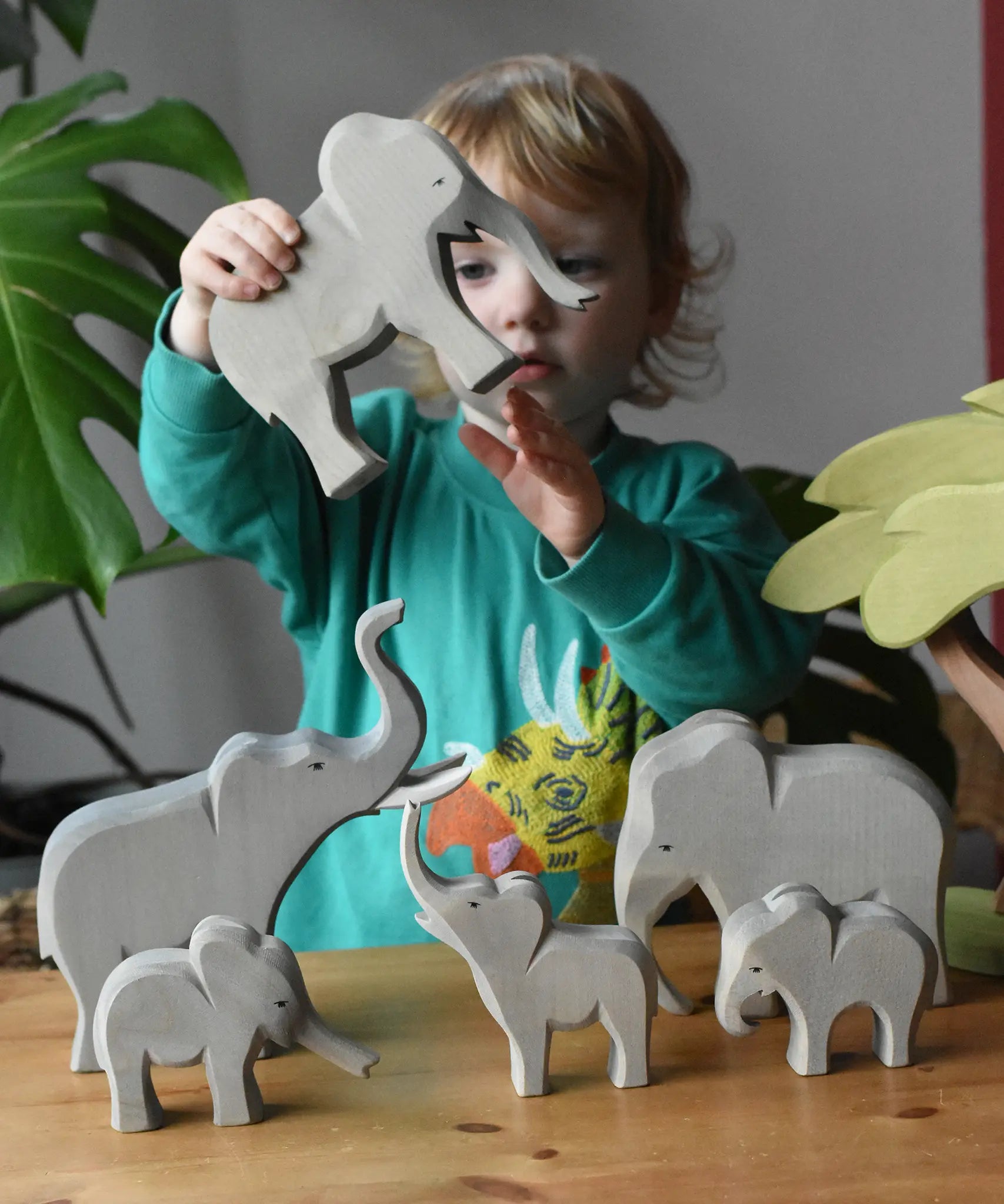 Collection of Ostheimer elephants wooden toy figures in a small world play scene with a child holding the trumpeting bull elephant.