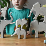 Collection of Ostheimer elephants wooden toy figures in a small world play scene with a child holding the small trumpeting elephant.