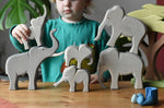 Collection of Ostheimer elephants wooden toy figures in a small world play scene with a child holding the small trumpeting elephant.
