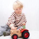 Child playing with the Ostheimer x Fagus wooden tractor and trailer indoors, with the farmer figure seated in the tractor.