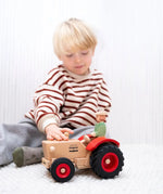 Child playing with the Ostheimer x Fagus wooden tractor and trailer indoors, with the farmer figure seated in the tractor.