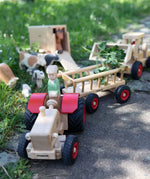 Ostheimer x Fagus wooden toy tractor pulling a Fagus trailer through an outdoor farm play scene with Ostheimer animals and wooden farm vehicles.