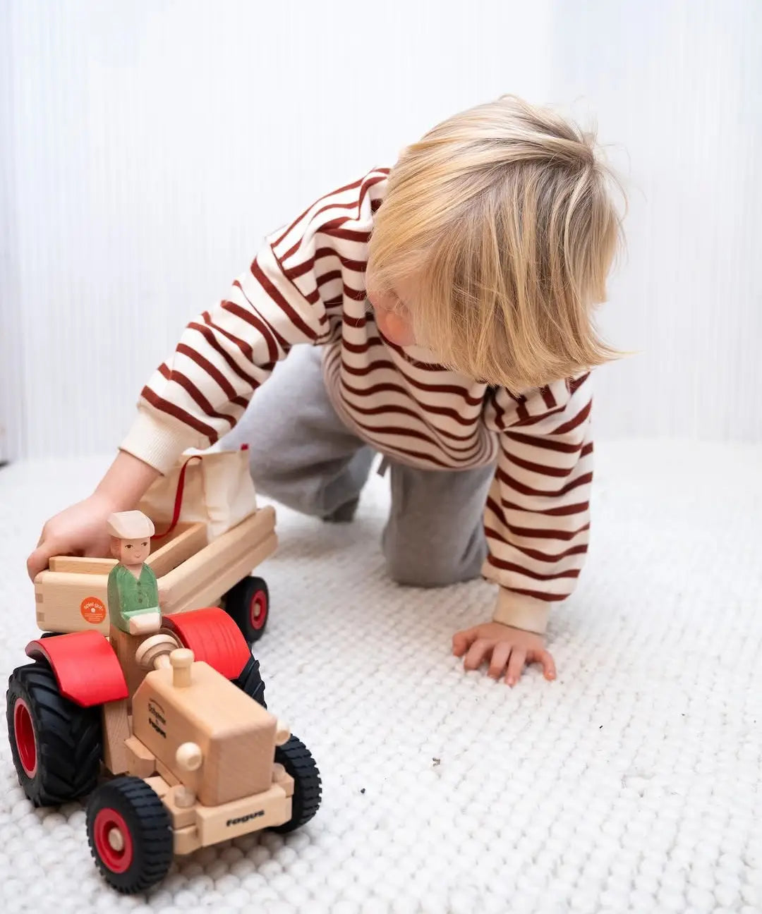 Child pushing the Ostheimer x Fagus wooden tractor indoors, with the Ostheimer farmer figure seated on the tractor.
