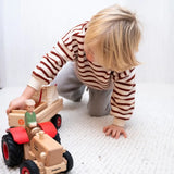 Child pushing the Ostheimer x Fagus wooden tractor indoors, with the Ostheimer farmer figure seated on the tractor.