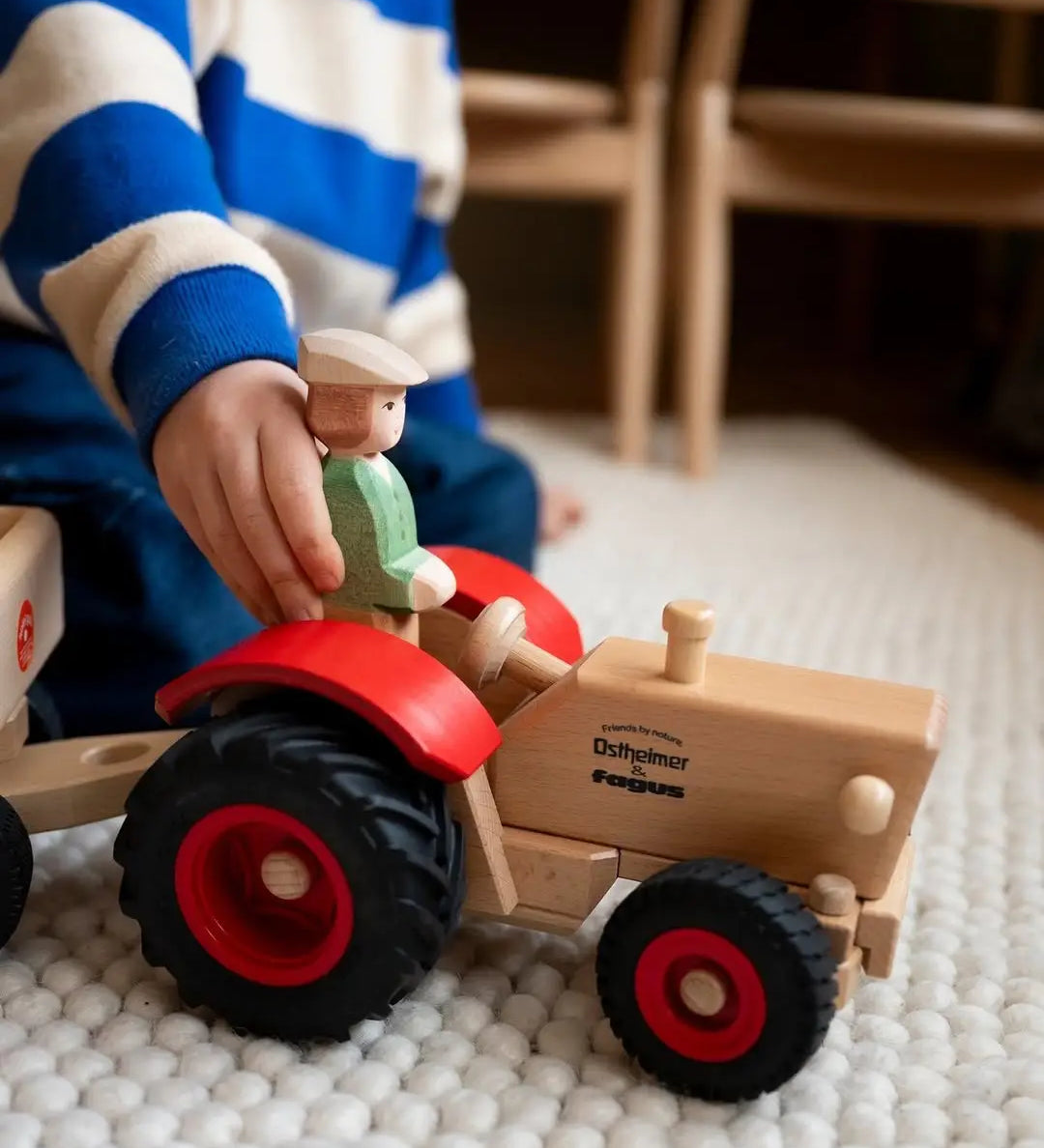 Child placing the Ostheimer farmer figure into the Ostheimer x Fagus wooden toy tractor with red mudguards and large black wheels.
