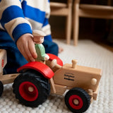 Child placing the Ostheimer farmer figure into the Ostheimer x Fagus wooden toy tractor with red mudguards and large black wheels.