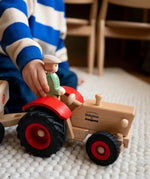 Child placing the Ostheimer farmer figure into the Ostheimer x Fagus wooden toy tractor with red mudguards and large black wheels.