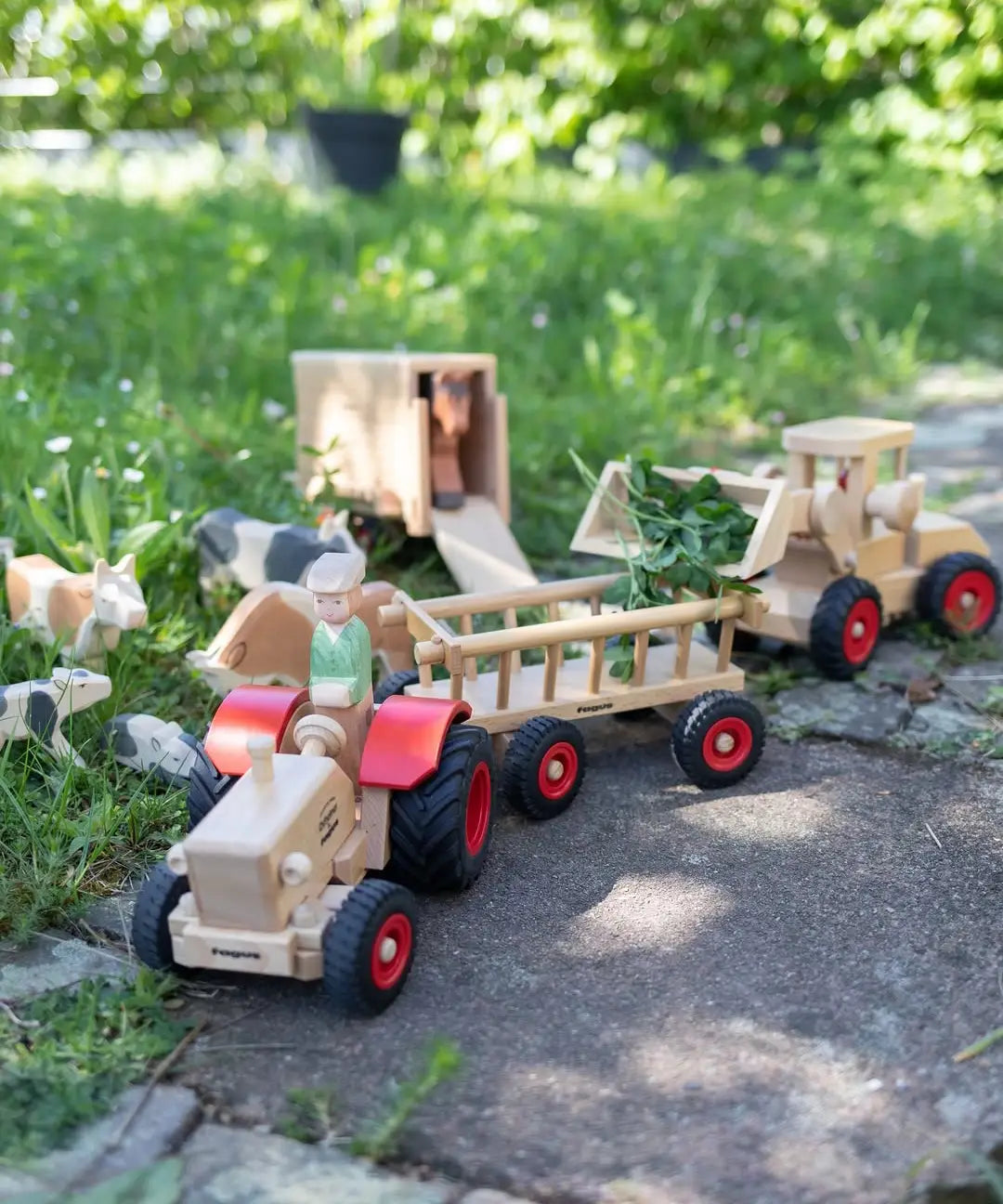 Ostheimer x Fagus wooden toy tractor pulling a Fagus trailer filled with leaves through a farmyard play scene with wooden animals.