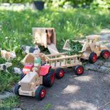 Ostheimer x Fagus wooden toy tractor pulling a Fagus trailer filled with leaves through a farmyard play scene with wooden animals.