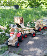 Ostheimer x Fagus wooden toy tractor pulling a Fagus trailer filled with leaves through a farmyard play scene with wooden animals.