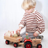 Child loading wooden sacks and vegetables into a Fagus trailer attached to the Ostheimer x Fagus toy tractor.