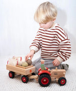 Child loading wooden sacks and vegetables into a Fagus trailer attached to the Ostheimer x Fagus toy tractor.