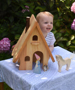 A child standing behind an Ostheimer Fairy Tale wooden dolls house. A medieval princess, cat and horse figures are placed in front of the house. These wooden figures are part of a large range of expertly hand crafted, Waldorf inspired, wooden toys here at Babipur.