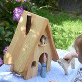 An Ostheimer fairy tale dolls house placed on a small table outdoors. A young child is standing in front of the house holding a white horse. 
These wooden figures are part of a large range of expertly hand crafted, Waldorf inspired, wooden toys here at Babipur. 