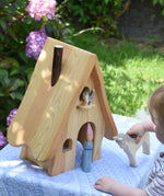 An Ostheimer fairy tale dolls house placed on a small table outdoors. A young child is standing in front of the house holding a white horse. 
These wooden figures are part of a large range of expertly hand crafted, Waldorf inspired, wooden toys here at Babipur. 