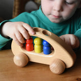 Ostheimer family van push along wooden toy with three people peg dolls. Child is pushing it along a wooden surface.