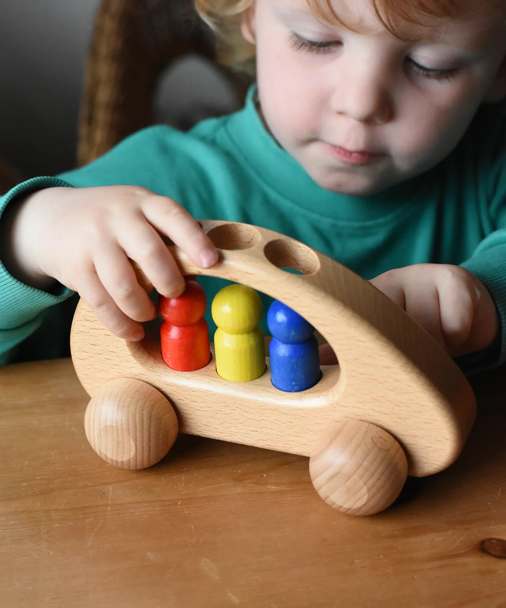 Ostheimer family van push along wooden toy with three people peg dolls. Child is pushing it along a wooden surface.
