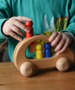 Child placing the red peg doll into the slot on the Ostheimer family van push along wooden toy.