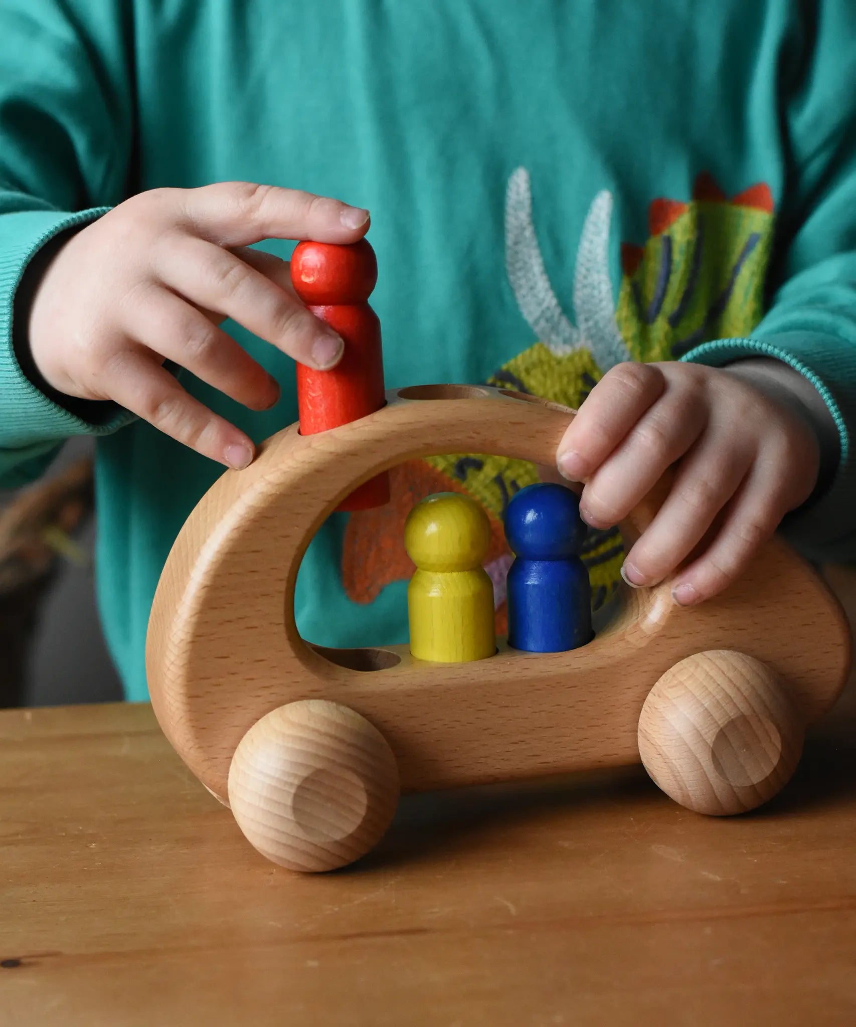 Child placing the red peg doll into the slot on the Ostheimer family van push along wooden toy.