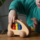 Ostheimer family van push along wooden toy with three people peg dolls. Child is pushing it along a wooden surface.