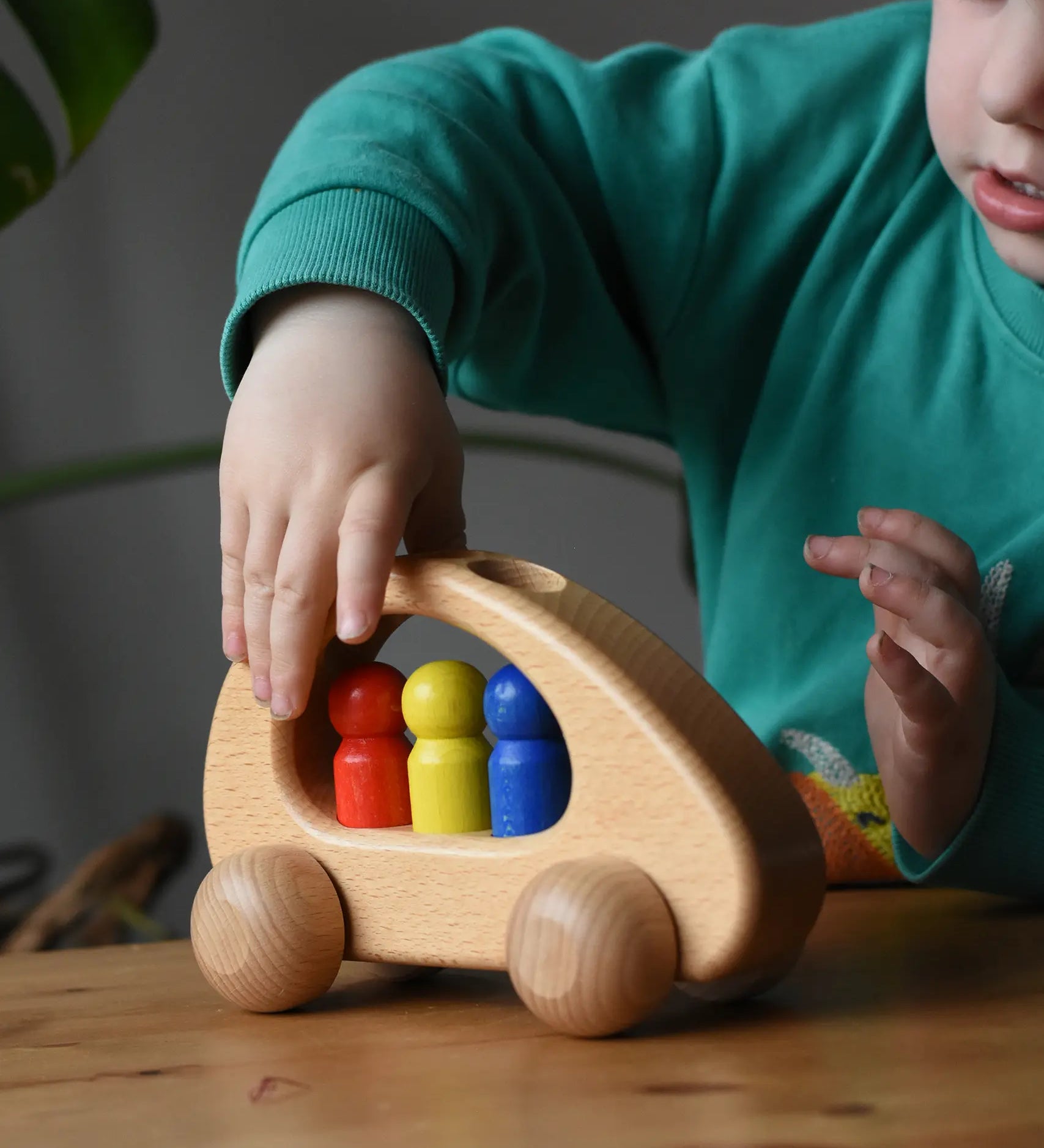 Ostheimer family van push along wooden toy with three people peg dolls. Child is pushing it along a wooden surface.