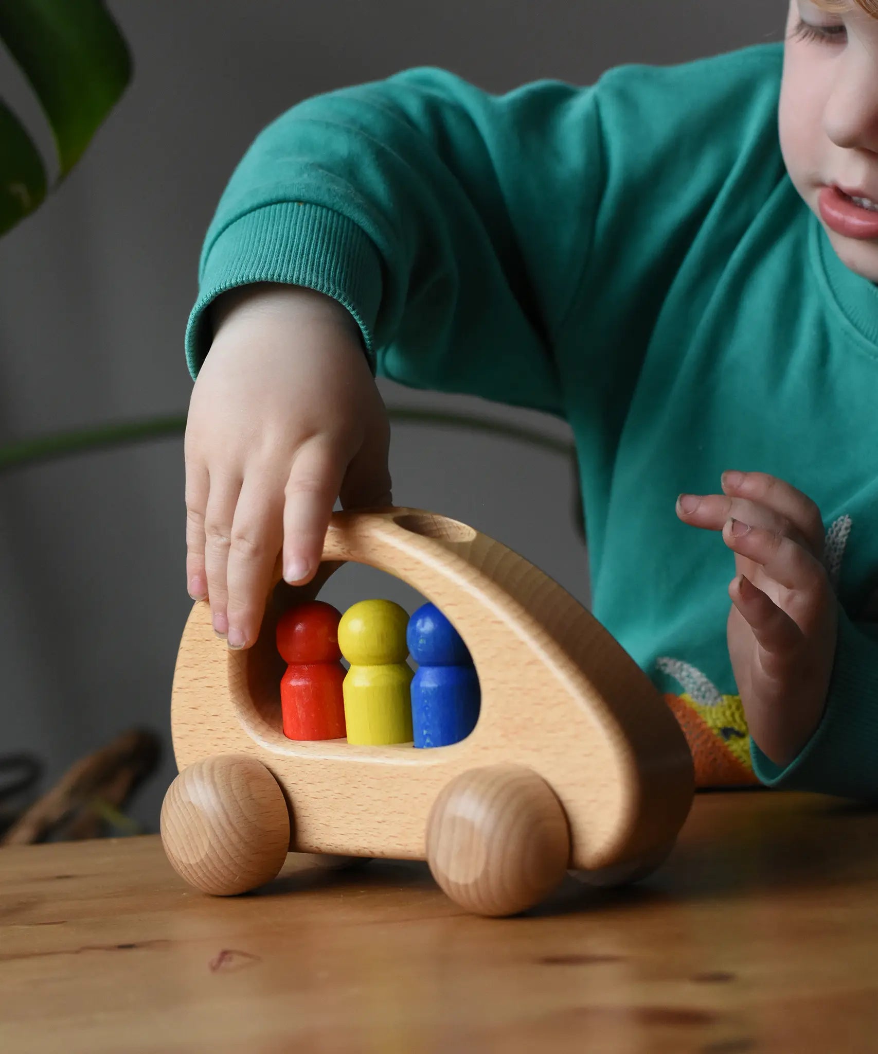 Ostheimer family van push along wooden toy with three people peg dolls. Child is pushing it along a wooden surface.