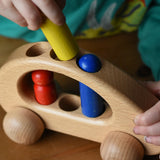 Close up of a child's hand placing the yellow peg doll into the circular slots in the Ostheimer family van push along wooden toy.