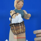 An Ostheimer Farmer Woman handcrafted wooden toy figure placed on a snow covered surface in the Babipur garden. The wooden toy figure is holding a small kraul basket filled with snow with it's pose-able arms. These wooden figures are part of a large range of expertly hand crafted, Waldorf inspired, wooden toys here at Babipur.
