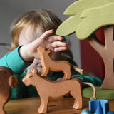 Ostheimer cub placed on a female lioness wooden toy figure with a child reaching for the cub figure in a small world play scene with the African tree.