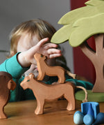 Ostheimer cub placed on a female lioness wooden toy figure with a child reaching for the cub figure in a small world play scene with the African tree.