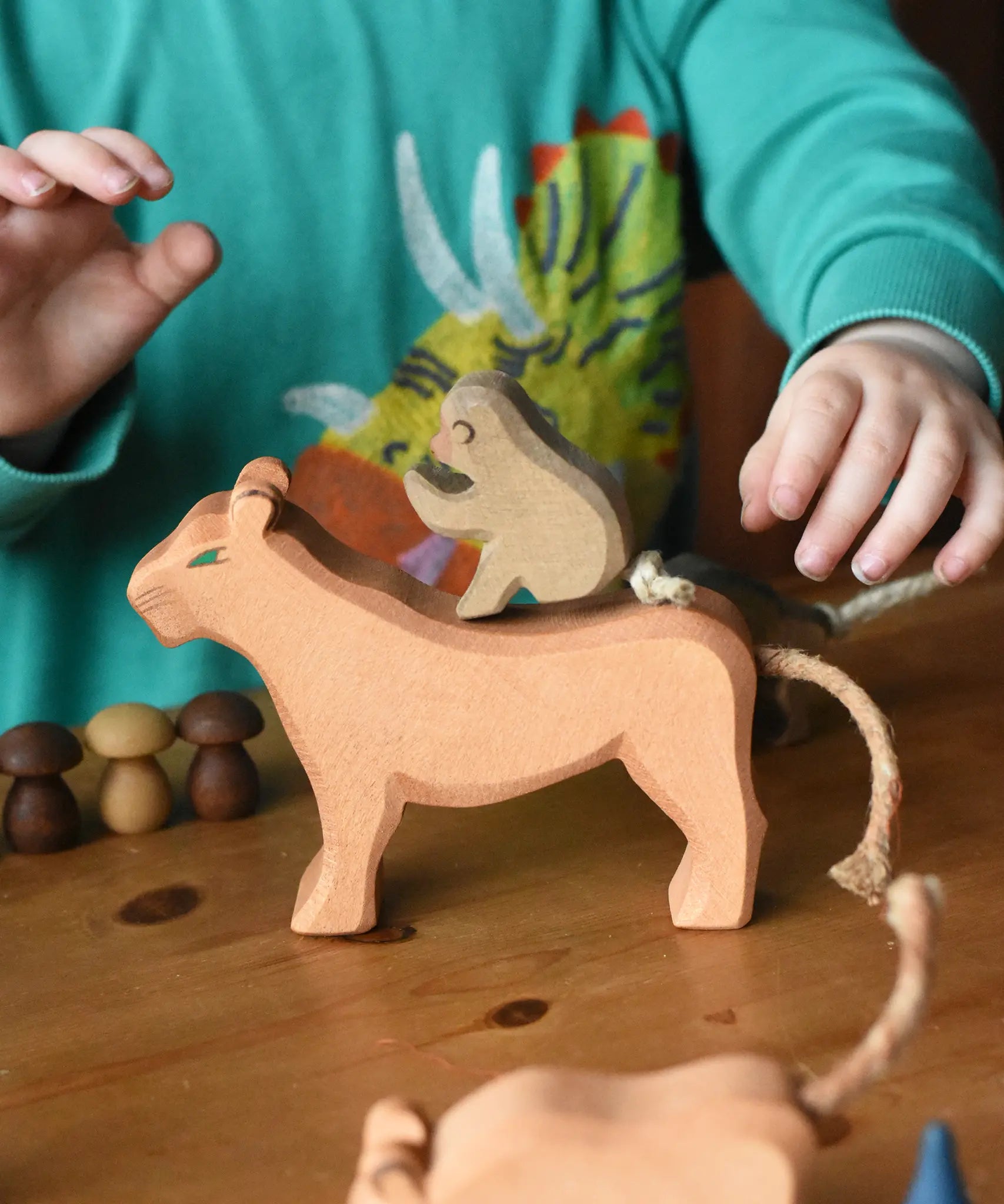 Ostheimer sitting baboon wooden toy figure placed on a female lioness figure. Child's hand reaching or the tail.