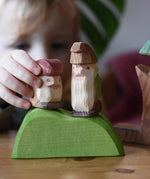 Close up of a child playing with two Ostheimer wooden dwarf figures placing them n a green bush piece. 