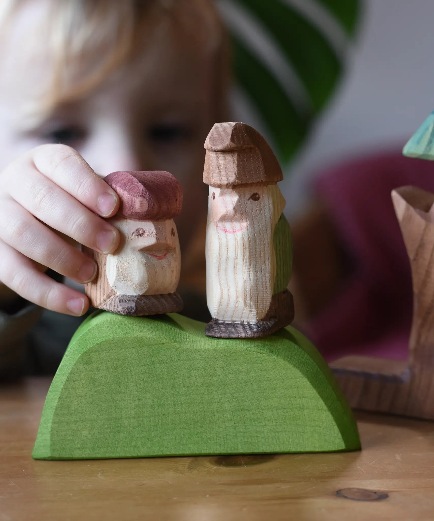 Close up of a child playing with two Ostheimer wooden dwarf figures placing them n a green bush piece. 