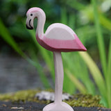 An Ostheimer flamingo bird placed on a mossy surface outdoors, blades of grass can be seen blurred in the background. This expertly hand crafted wooden figure is part of a large range of wooden toys here at Babipur.