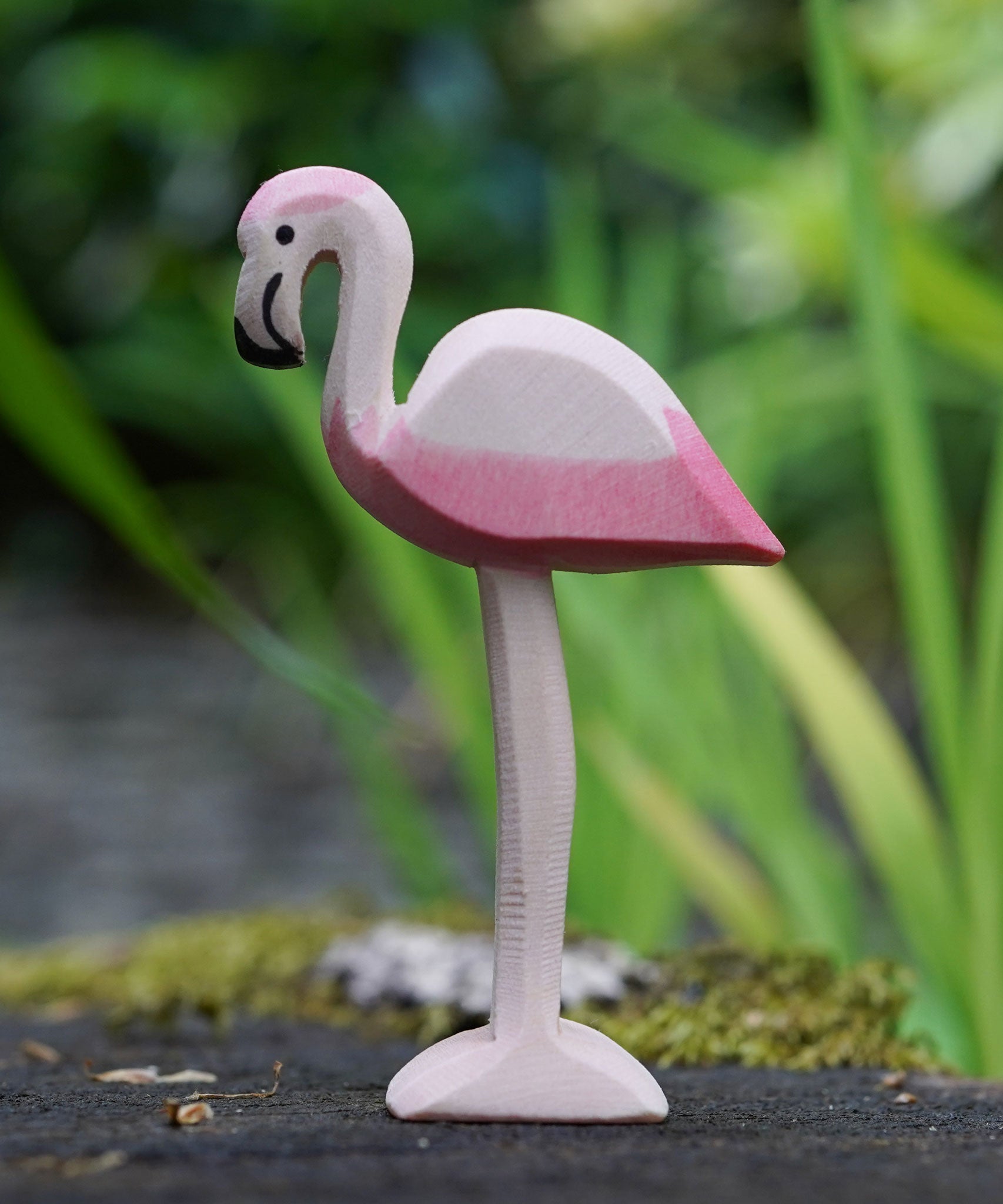 An Ostheimer flamingo bird placed on a mossy surface outdoors, blades of grass can be seen blurred in the background. This expertly hand crafted wooden figure is part of a large range of wooden toys here at Babipur.