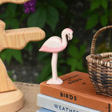 An Ostheimer flamingo wooden toy figure placed on a pile of books. An Otheimer bird tree can be seen in the background.