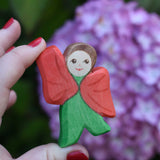 An Ostheimer hand made and hand painted wooden poppy Flower Child figure toy held in an adult's hand for scale. These flower child wooden figures are part of a wide range of expertly hand crafted wooden toys here at Babipur. 