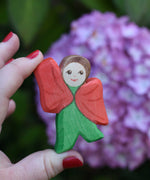An Ostheimer hand made and hand painted wooden poppy Flower Child figure toy held in an adult's hand for scale. These flower child wooden figures are part of a wide range of expertly hand crafted wooden toys here at Babipur. 