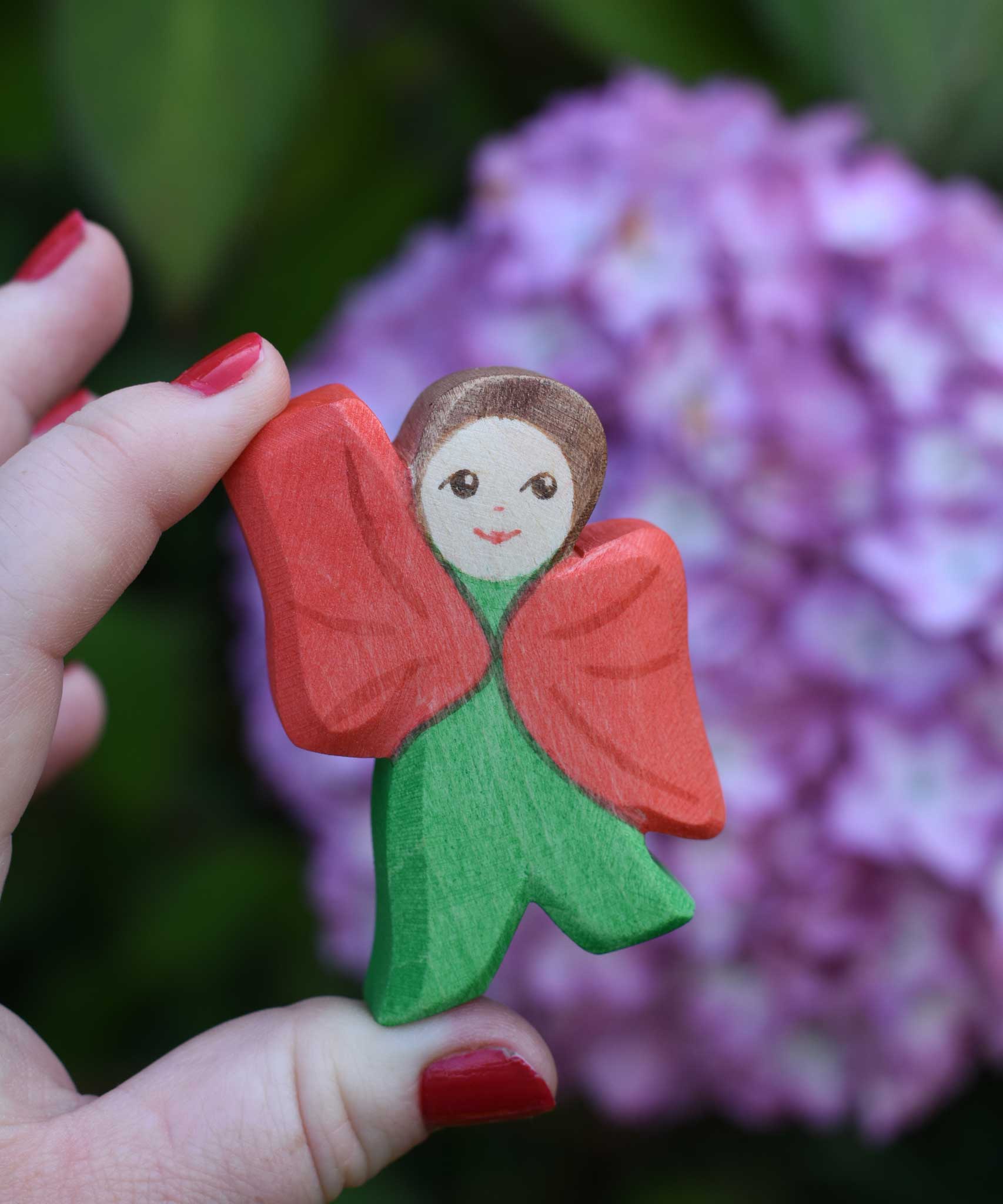 An Ostheimer hand made and hand painted wooden poppy Flower Child figure toy held in an adult's hand for scale. These flower child wooden figures are part of a wide range of expertly hand crafted wooden toys here at Babipur. 