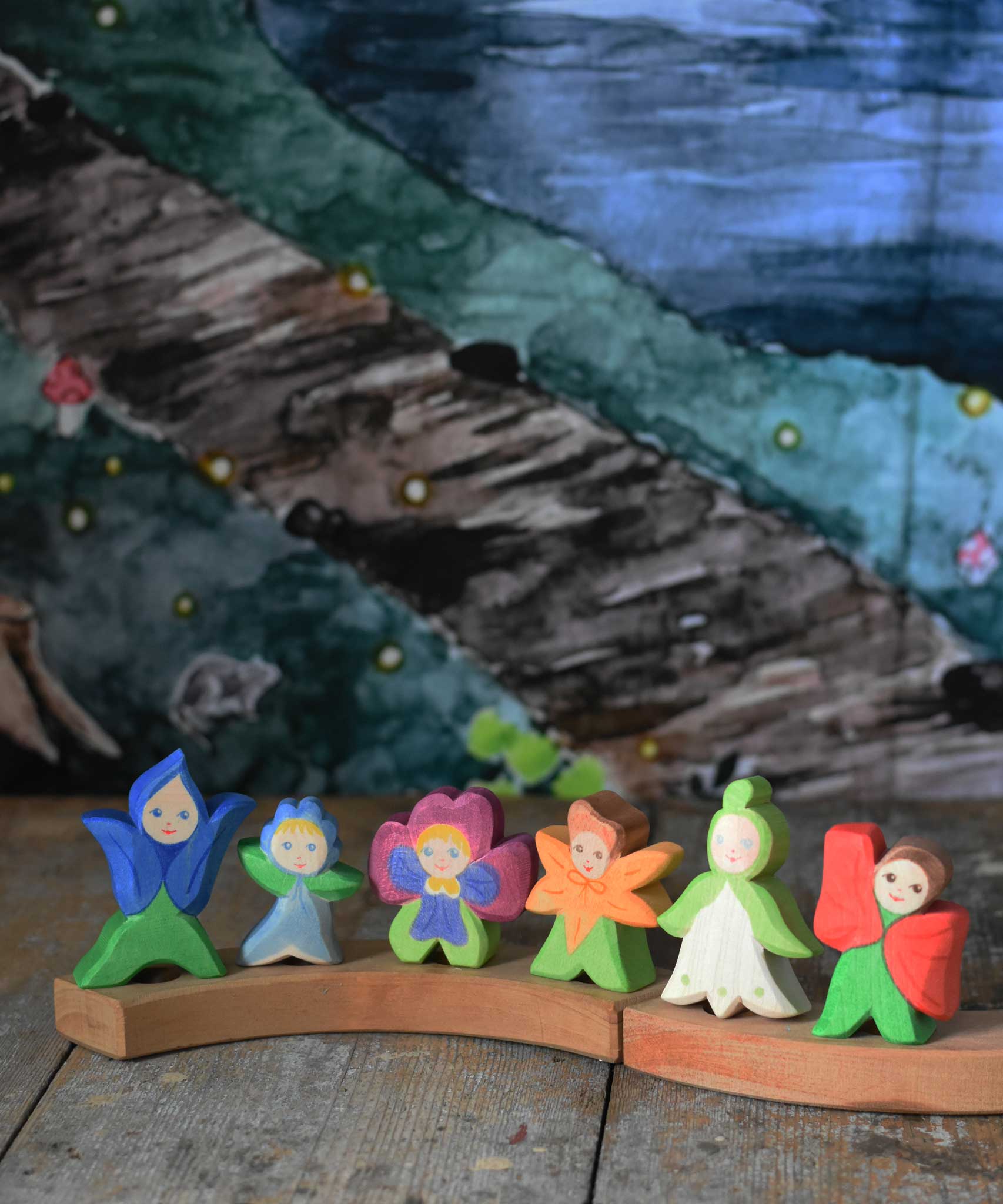 A collection of 6 Ostheimer wooden flower child figures placed on a natural Grimm's celebration ring. The six flower child figures include the gentian, forget-me-not, pansy, calendula, snowdrop and poppy.