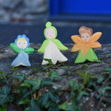 Three Ostheimer hand made and hand painted wooden forget-me-not, snowdrop and calendula Flower Child figure toys placed on a stone wall outdoors. These flower child wooden figures are part of a wide range of expertly hand crafted wooden toys here at Babipur. 