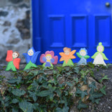 Six Ostheimer hand made and hand painted wooden poppy Flower Child figure toys placed on a stone wall outdoors. The six flower child figures include the gentian, forget-me-not, pansy, calendula, snowdrop and poppy. These flower child wooden figures are part of a wide range of expertly hand crafted wooden toys here at Babipur. 
