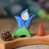 An Ostheimer hand made and hand painted wooden Gentian Flower Child figure toy placed on a natural Grimm's celebration ring. These flower child wooden figures are part of a wide range of expertly hand crafted wooden toys here at Babipur. 